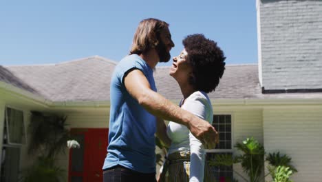 feliz pareja de raza mixta abrazándose cerca de una nueva casa de apartamentos