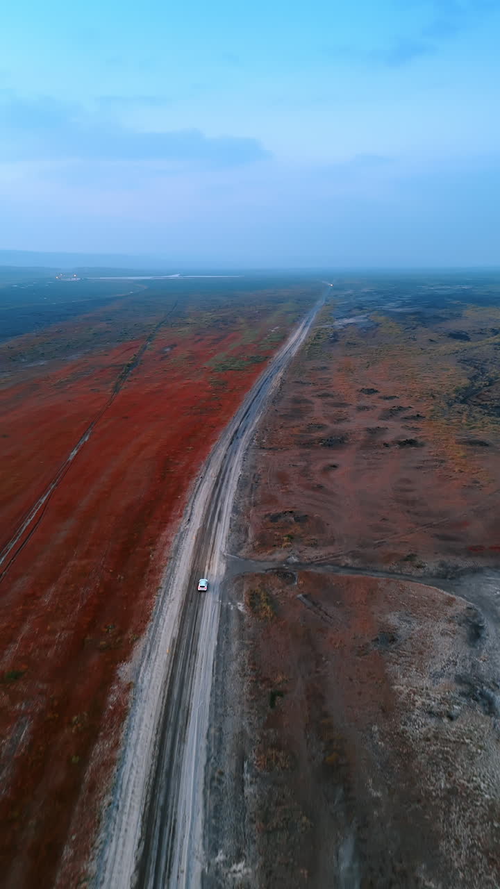 White car moving quickly by the ground road. Aerial perspective on the unrealistic landscape of Iceland. Vertical video.