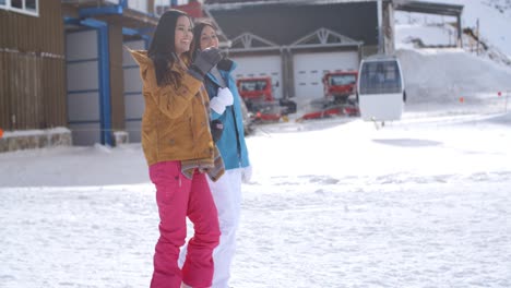 two young women walking through snow at a resort