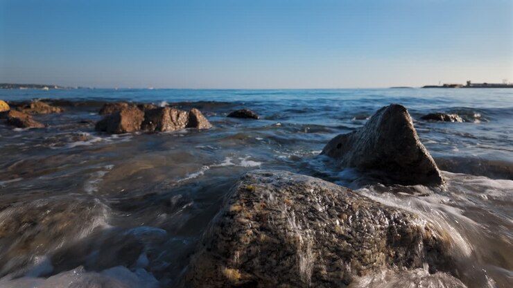 Vista di onde marine che lambiscono dolcemente la costa rocciosa sotto un cielo azzurro limpido