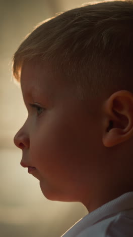 little kid looks calmly standing against bright light. boy rests in glamping tent in evening closeup. tired child after activities at resort side view