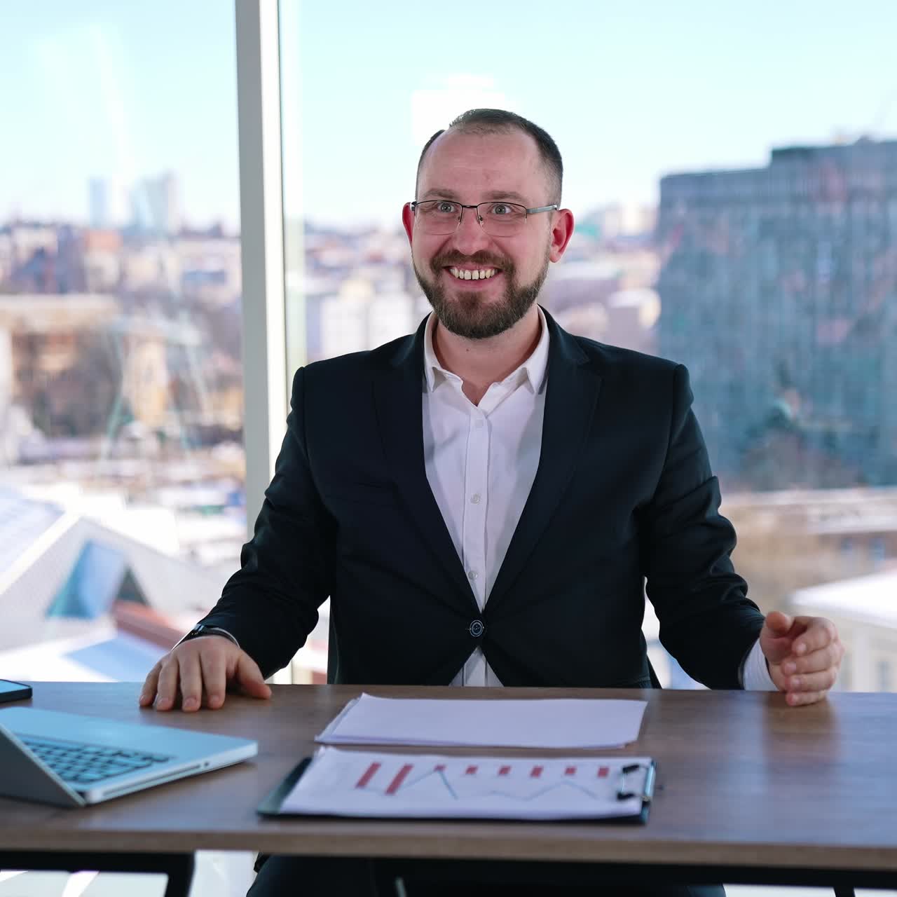 Astonished businessman at workplace. Smiling office worker sitting at the table with a laptop on window background with city view