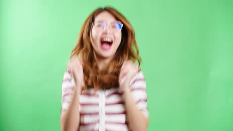 cheerful young asian woman with eyeglasses raising hands up, shaking and having fist pump from happiness, smiling woman face, green screen background