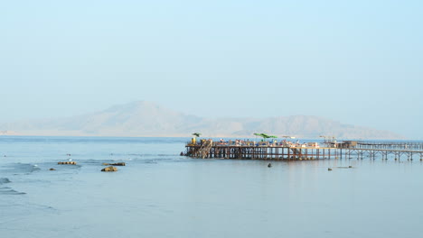 Pier-with-tourists-by-the-beach,-mountains-in-background-at-Sharm-El-Sheikh