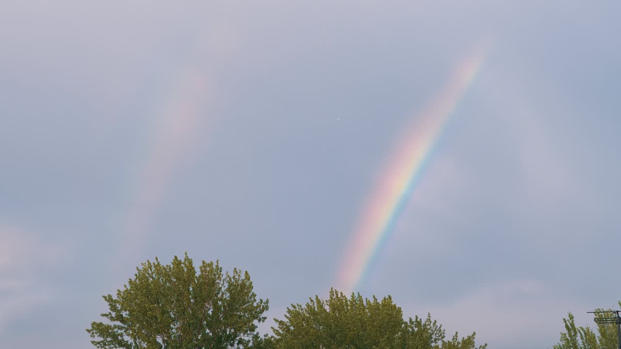 aparición de un doble arco iris brillante en el horizonte a través de nubes grises en el cielo. 4k