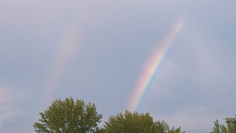 aparición de un doble arco iris brillante en el horizonte a través de nubes grises en el cielo. 4k