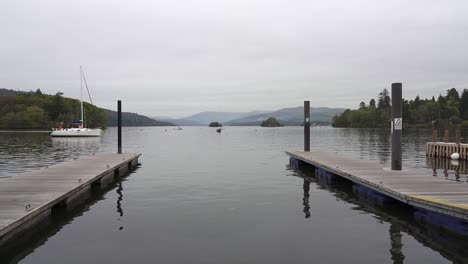 a small sailing yacht sails toward a jetty in a marina on the shores of lake windermere in the lake district, england, uk