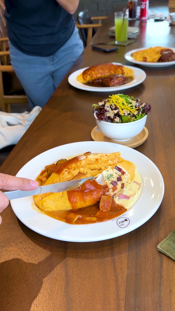 Un commensale usa un cucchiaio per mangiare omurice con salsa, luce intensa, ristorante informale, primo piano