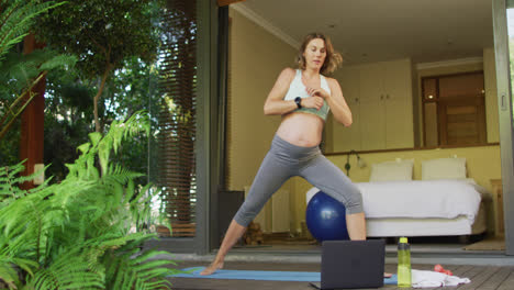 caucasian pregnant woman practicing yoga at home with online lessons