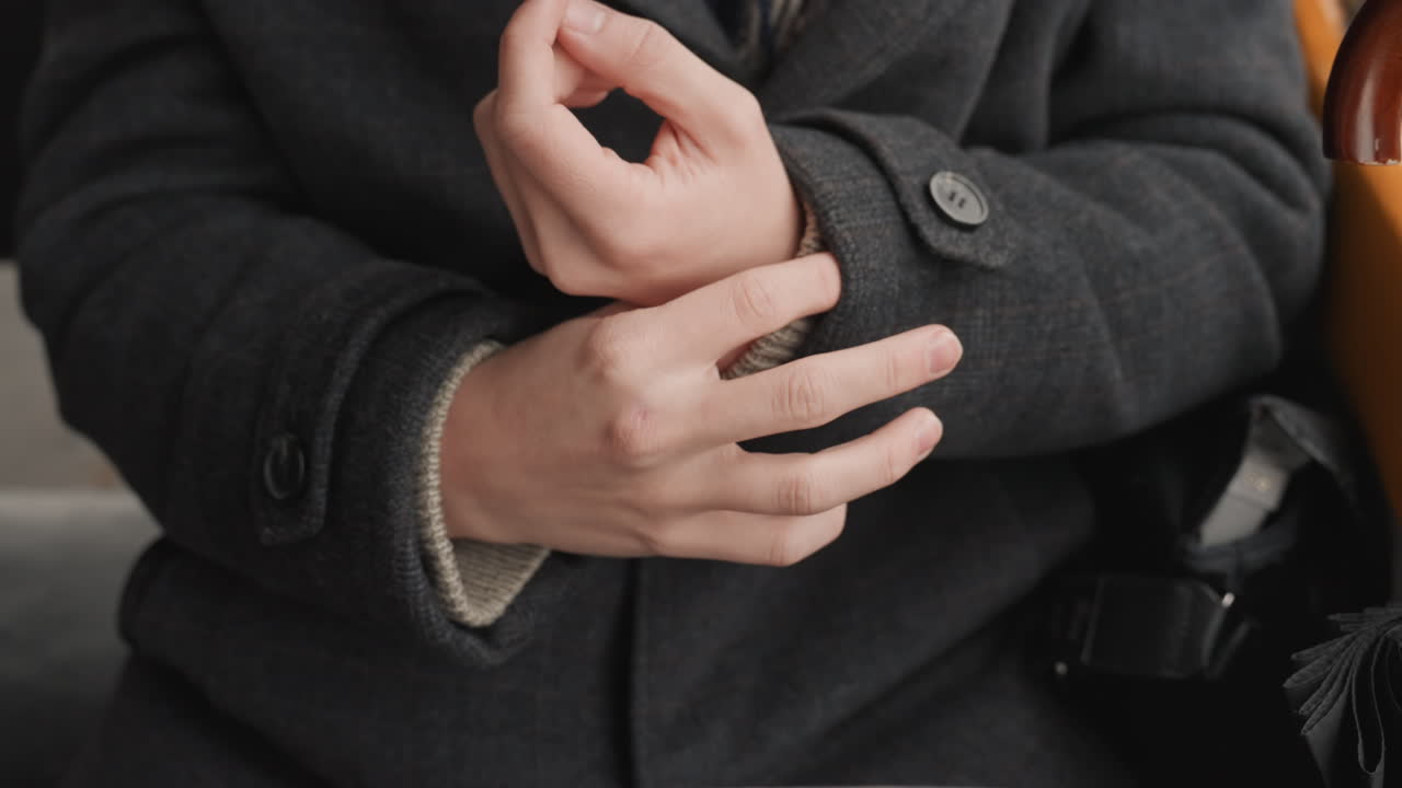 Closeup hands creator adjusting cuff, fidgeting with fingers and buttons microgestures include clasping, rubbing, interlacing as if planning next project wool coat texture, muted tones, seated