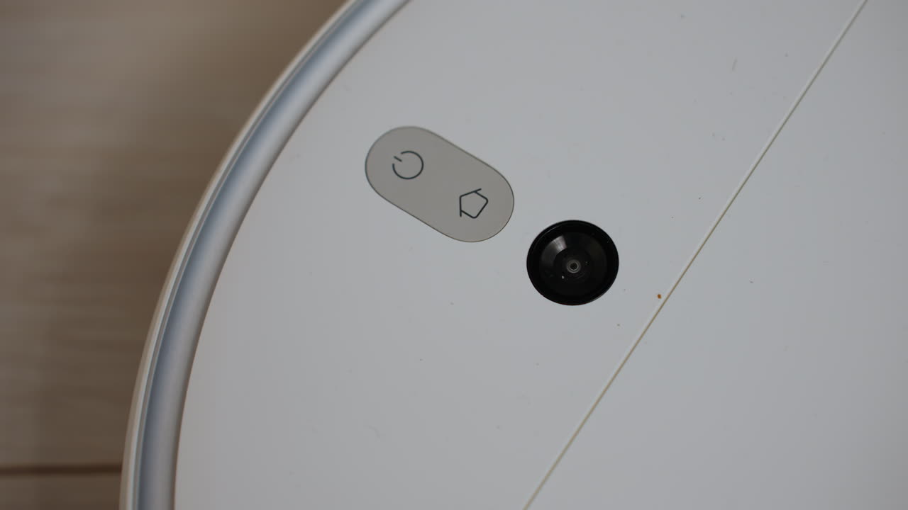 Detailed close up of robotic vacuum cleaner with glowing control buttons and lens while moving on wooden floor, showing modern smart cleaning appliance, advanced technology