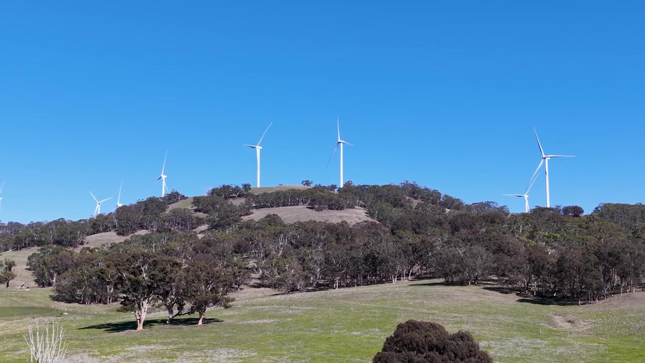 Turbine eoliche generano energia rinnovabile lungo colline rurali boscose sotto un cielo azzurro limpido