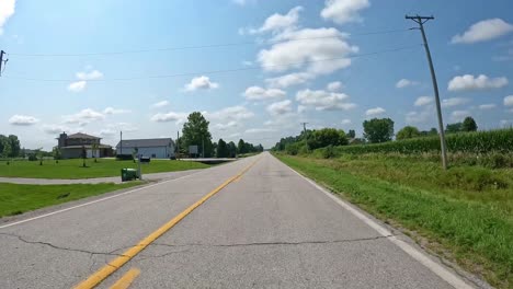 pov - driving on a rural county road past fertile fields in late summer in central iowa