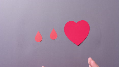 manos de una mujer caucásica protegiendo el corazón y gotas de sangre en fondo gris, cámara lenta
