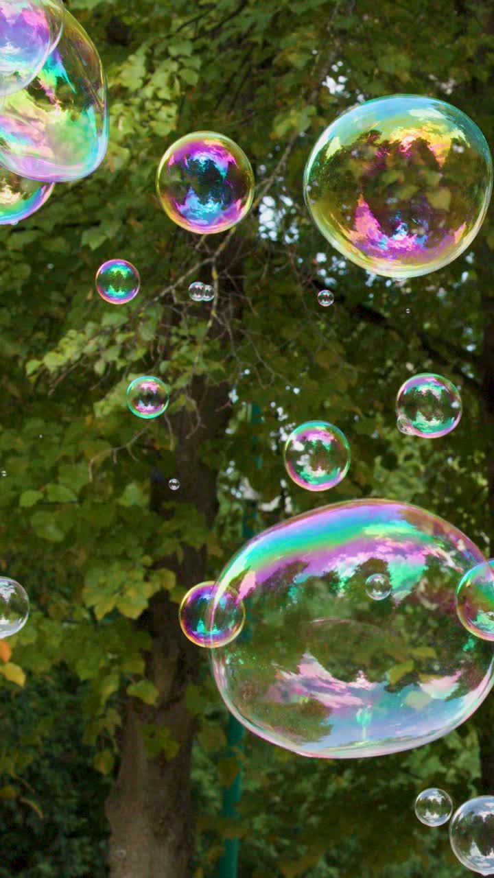 Bolle di sapone iridescenti e colorate fluttuano lentamente attraverso un parco con alberi verdi e vivaci alla luce del giorno