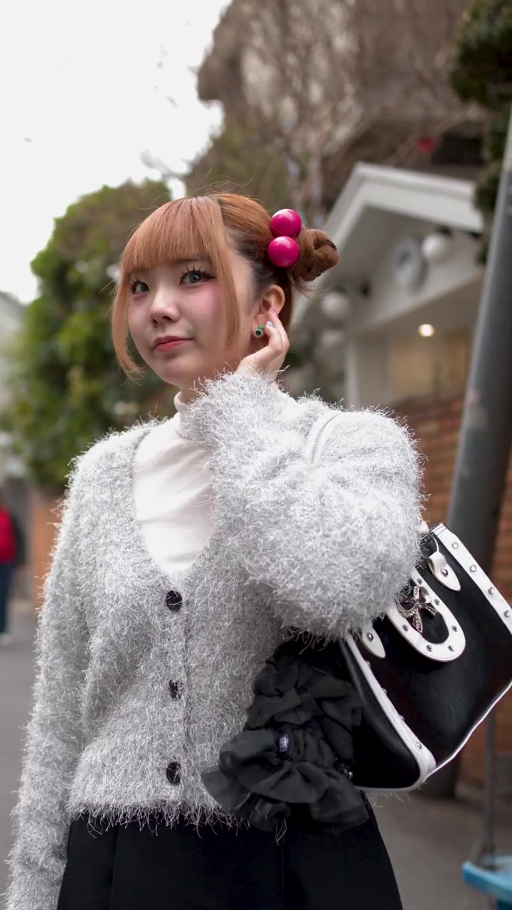 Una giovane donna elegante cammina per Harajuku, Tokyo, indossando un cardigan peloso e accessori per capelli