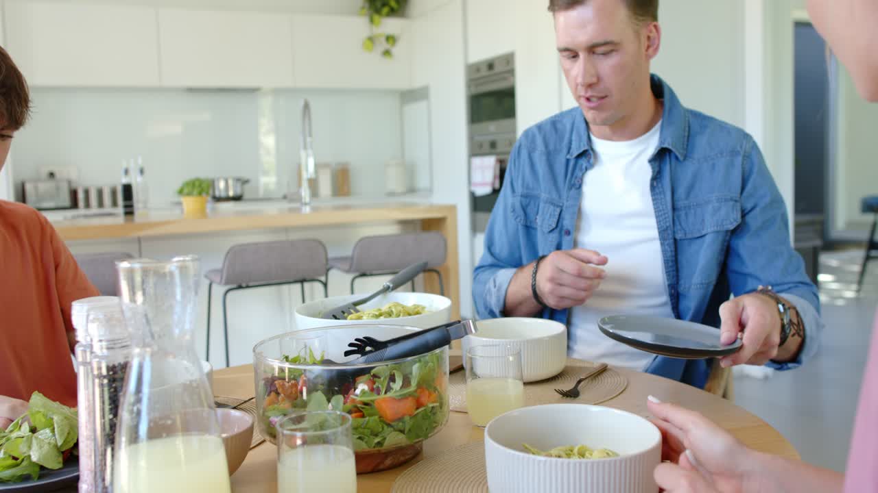 Family with youth starting meal, dishes arriving while man blue shirt using tongs to plate salad