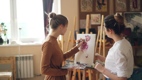 two young women painting flowers in an art studio