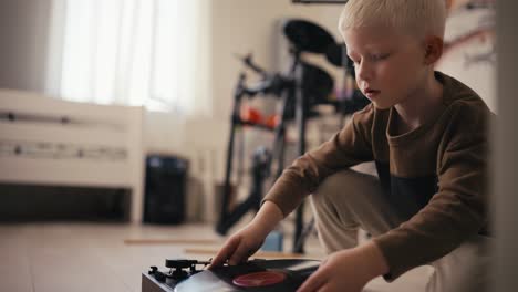 Close-up-shot-of-a-small-albino-boy-with-white-hair-puts-a-music-record-on-the-player-and-then-turns-it-on-and-listens-to-music-in-his-room.-Antiques-and-hobbies-of-a-little-albino-boy-at-home