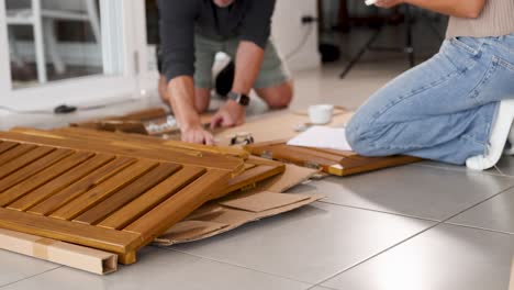 a couple assembles wooden furniture on a tiled floor, using instructions and tools, in a well-lit indoor setting