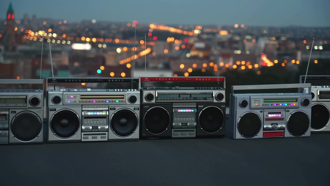 L'inquadratura centrale presenta tre boombox retrò su una sporgenza di un tetto, rivolti verso la fotocamera.