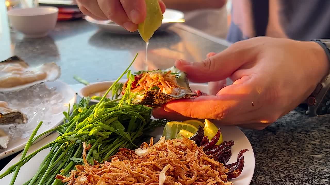 A close-up of lime being squeezed over a seafood platter with herbs and crispy toppings.