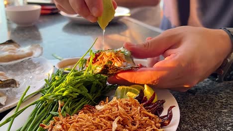 a close-up of lime being squeezed over a seafood platter with herbs and crispy toppings.