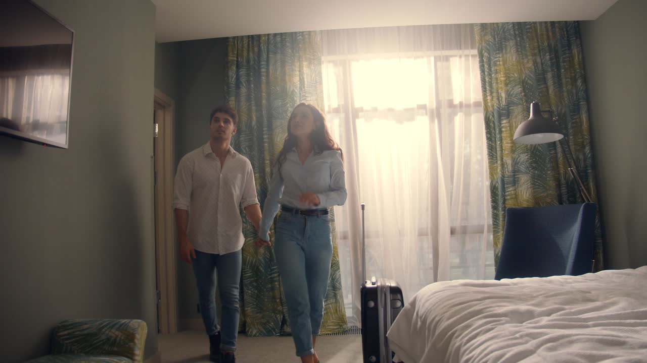 Cute couple holding hands in hotel room. Love couple falling bed in apartment.