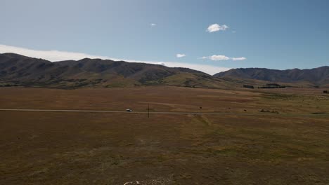 un coche aparcado al lado de la carretera de la pradera aislada bajo el sol, con la cordillera al fondo