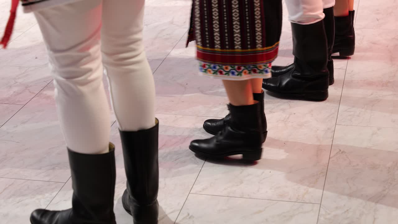 Filmato ravvicinato del gioco di gambe di ballerini folk rumeni che indossano stivali di pelle tradizionali durante uno spettacolo di danza culturale. Focus su movimento ritmico, passi e dettagli autentici del costume