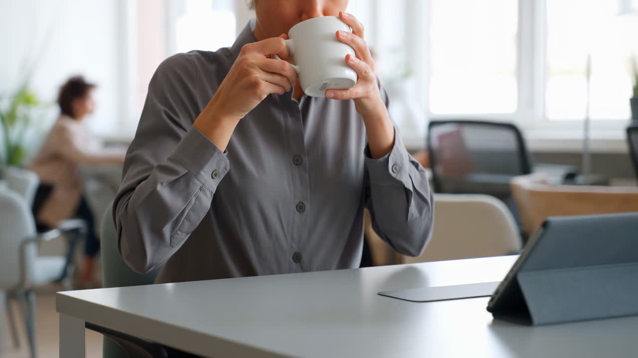 Kvinde drikker kaffe fra et hvidt krus på et kontor