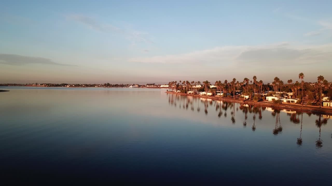 Drone che si allontana sull'acqua a Mission Bay all'alba rivelando palme e paesaggi costieri