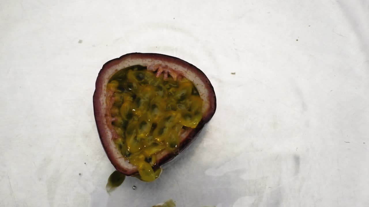 Ovenfra-udsigt af halv passionsfrugt, der falder ned i vandoverfladen i slowmotion, på hvid baggrund