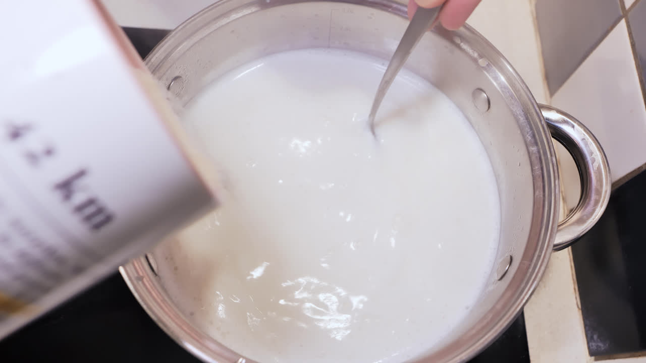 European man pours semolina into boiling milk with one hand while stirring