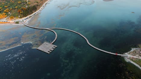 winding boardwalk over a vibrant turquoise lagoon in albania at sunset, aerial view