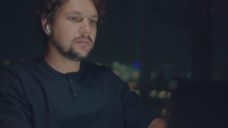 lose-up of the hands and face of a curly-haired man typing on a laptop