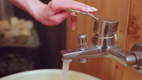 close up of person turning off water tap on sauna bathroom panel, chrome faucet detail, polished nail hand stopping water flow into basin, capturing tactile interaction and relaxation moment
