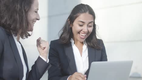 colegas de oficina alegres sentados afuera y usando una computadora portátil