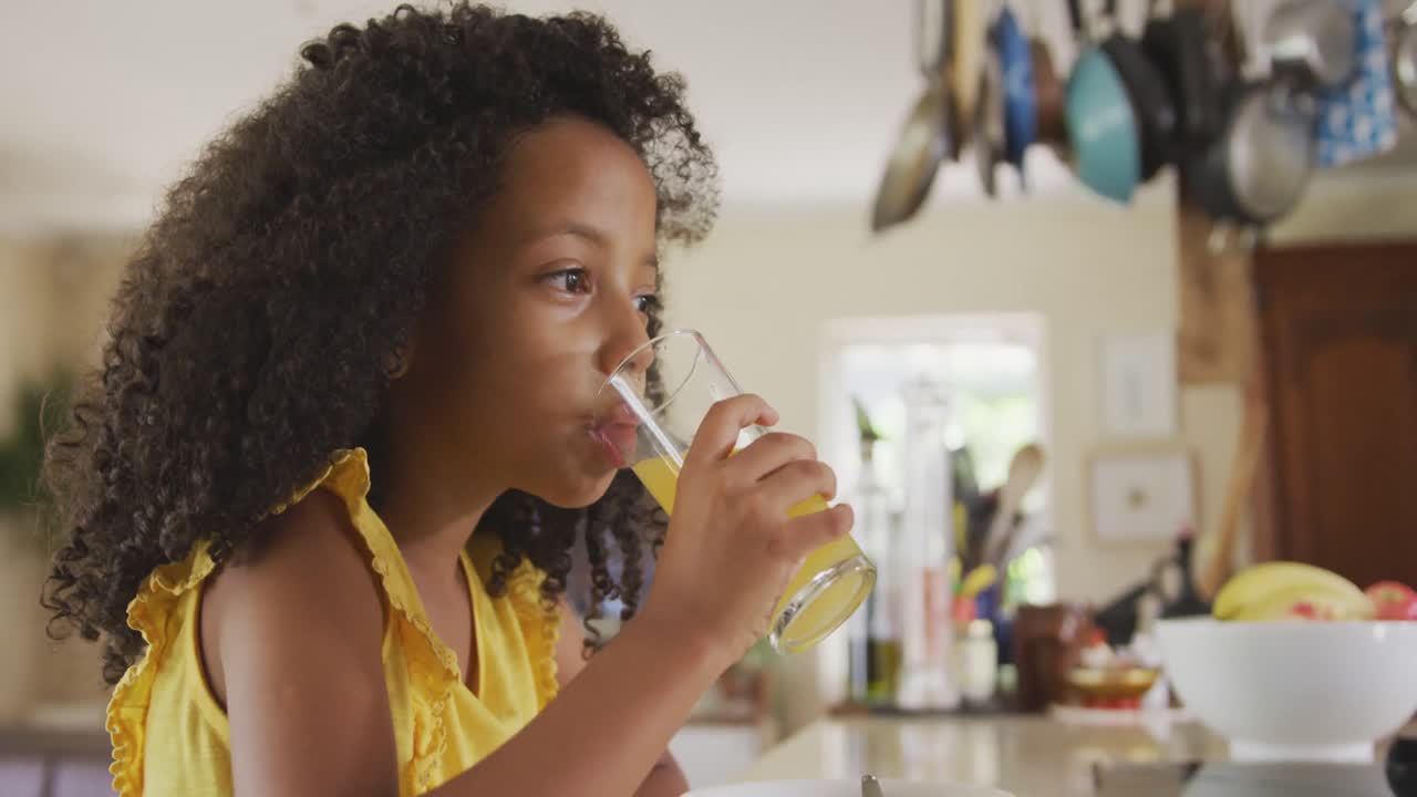 Vue de face d'une jeune fille afro-américaine buvant du jus le matin