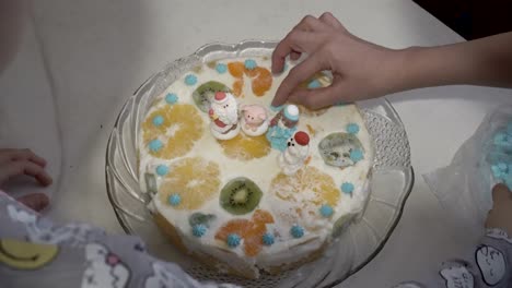 feliz familia, madre e hija, decorar pastel de navidad con crema blanca y estatuillas de frutas de santa claus y animales. el concepto de una fiesta familiar. de cerca. la vista desde la parte superior. 4k.