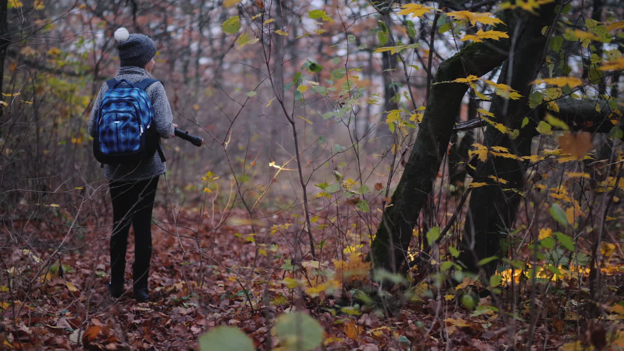 책가방을 뒤에 든 아이가 손전등을 들고 어두운 숲을 걷고 있다가 길을 잃다