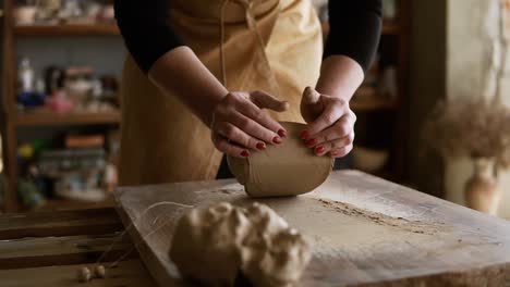 Close-up-footage-of-female-hands-with-beautiful-red-manicure-holding-clay-and-kneading-it-on-a-worktop.-Wearing-beige-apron.-Unrecognizable-person.-Overview.-Blurred-background