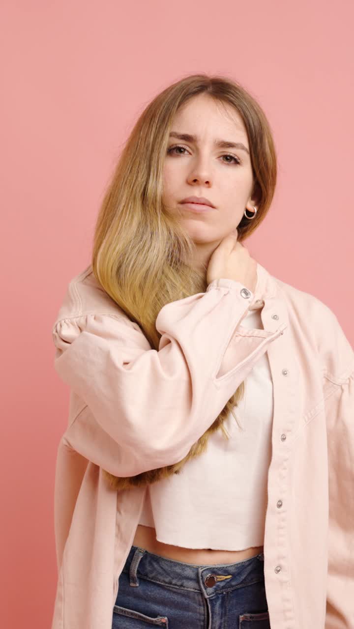 Young woman massaging neck on pink background