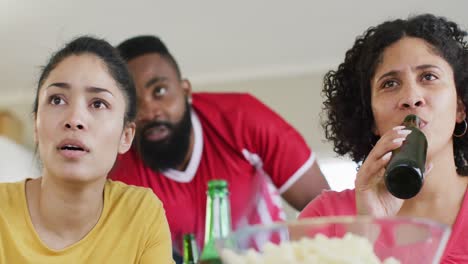 Diverse-female-and-male-friends-drinking-beer-watching-football-on-tv-at-home,-in-slow-motion