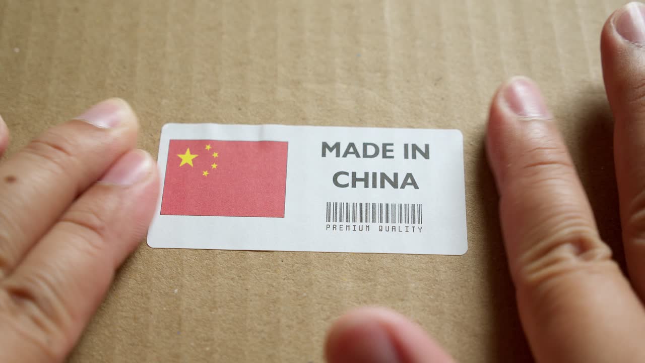 Hands applying MADE IN CHINA flag label on a shipping box with product premium quality barcode