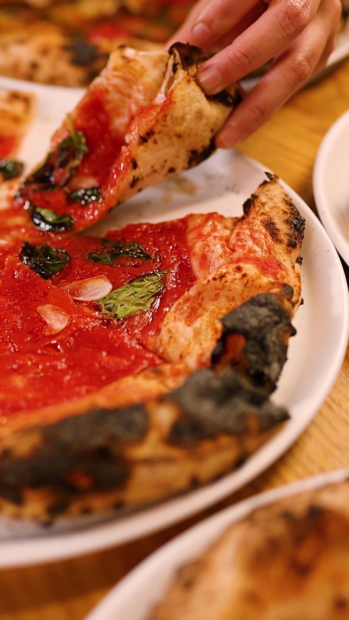 Närbild på en hand som lyfter en varm pizzabit från en vit tallrik
