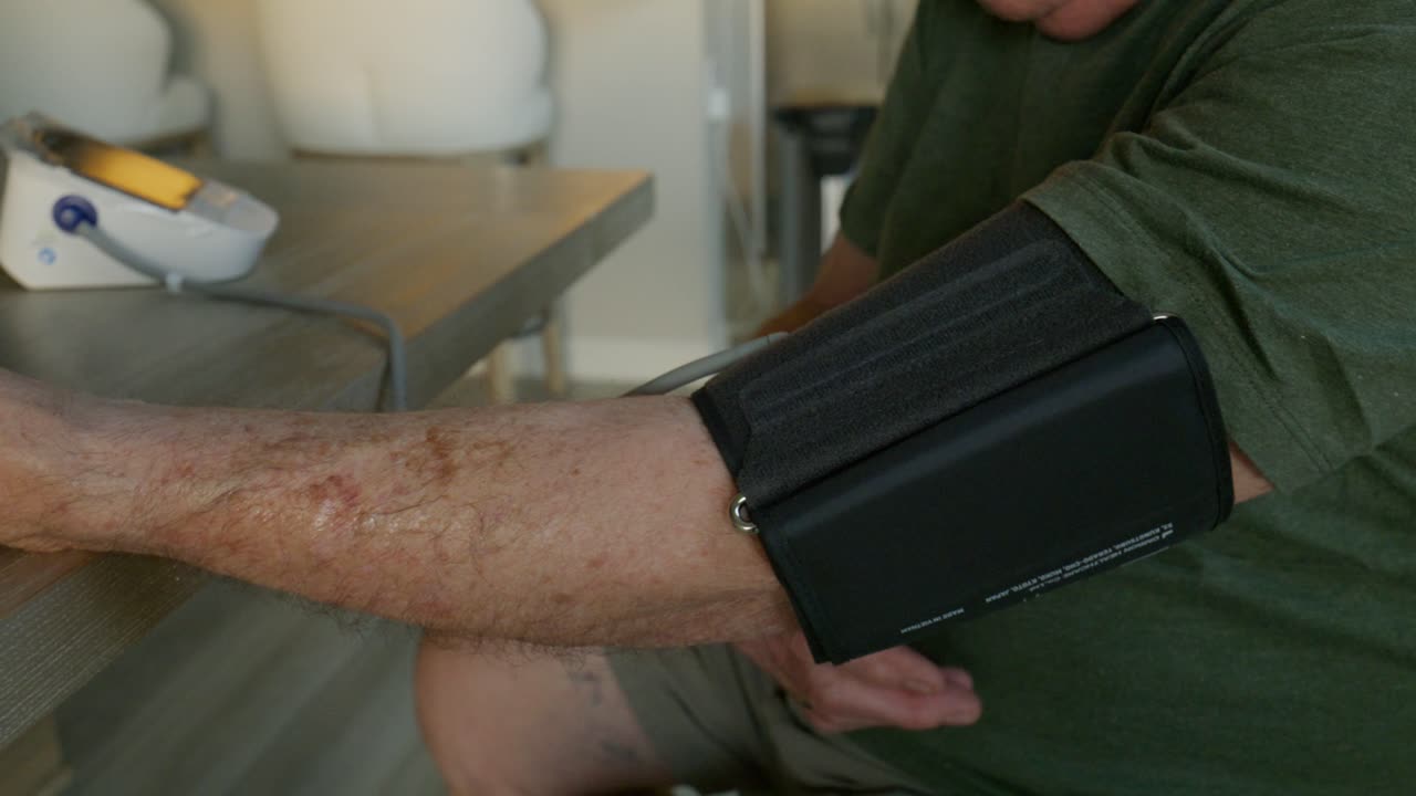 Un anziano si mette il bracciale per misurare la pressione sanguigna nel pomeriggio, primo piano che mostra le mani e la pelle anziane, ripresa lenta con slider.