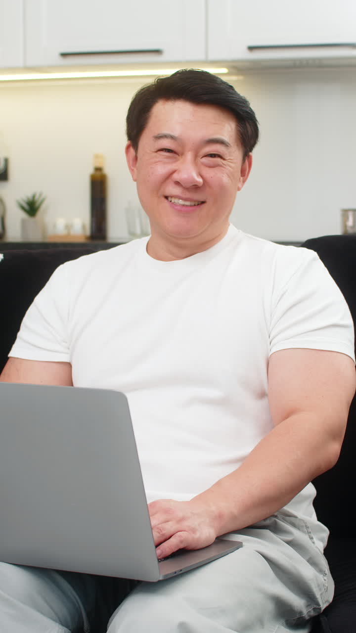 Asian man launches laptop for work logs in types quickly smiles with confidence ready to start tasks