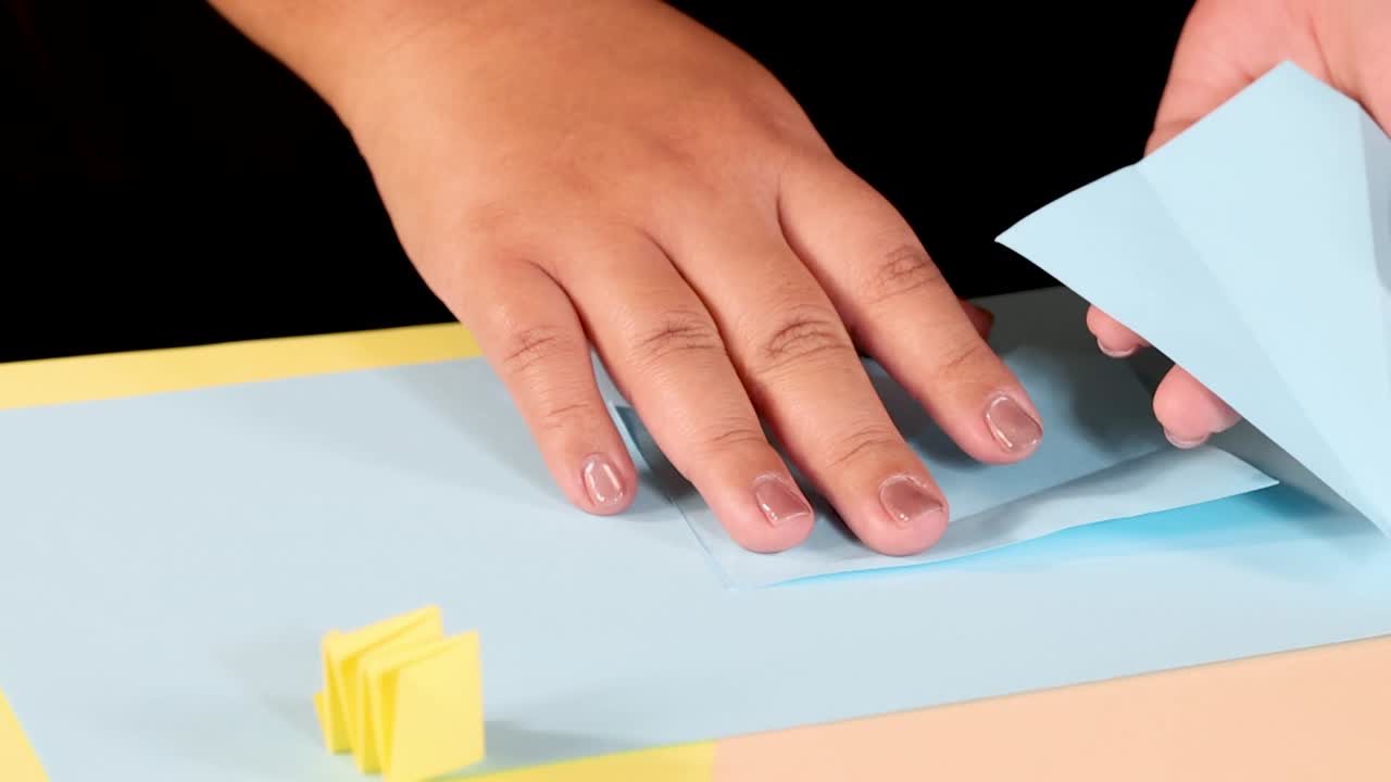 Mani che tagliano e piegano con cura carta azzurra su un piano di lavoro color pastello