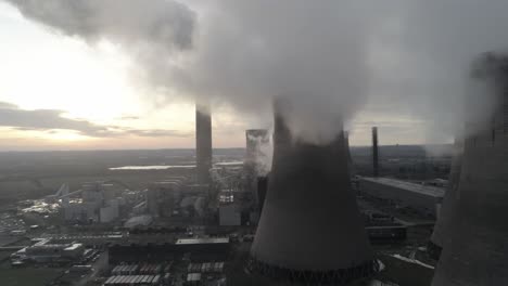 aerial shot of atmospheric power station cooling towers smoke steam emissions overlooking sunrise horizon